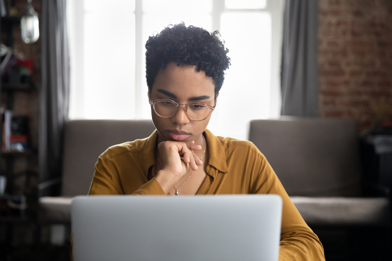Woman with short hair and yellow shirt searches the internet on a laptop.